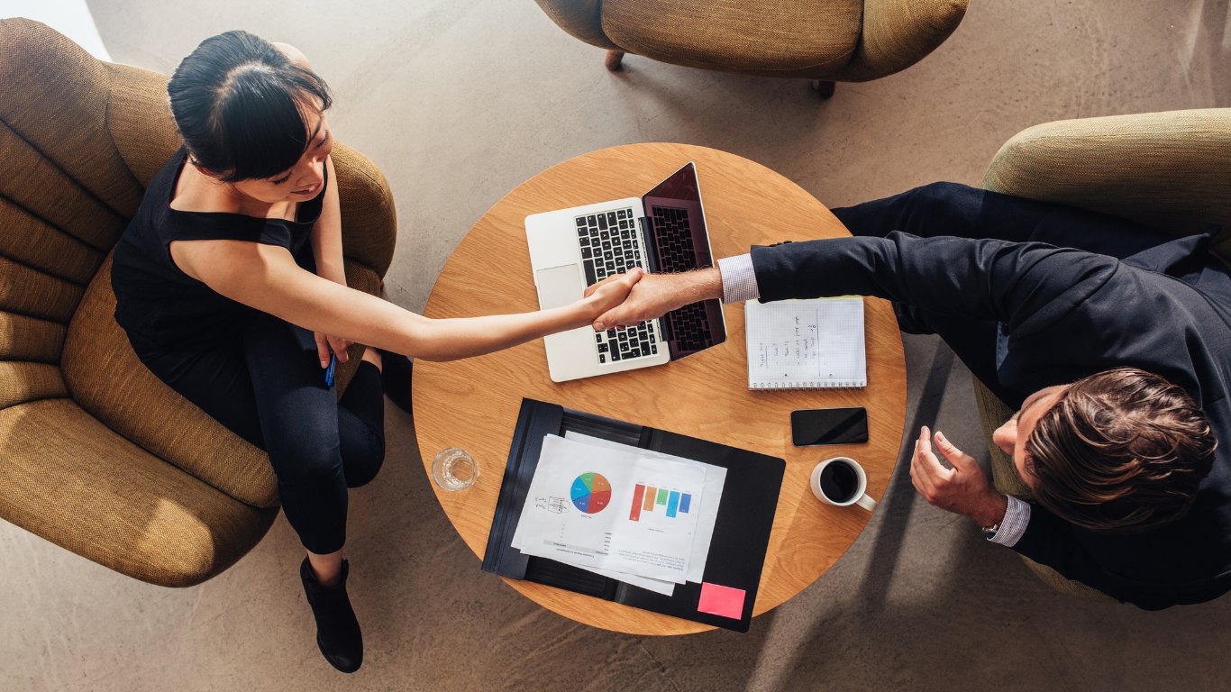 Two professionals shaking hands across a table, seen from above
